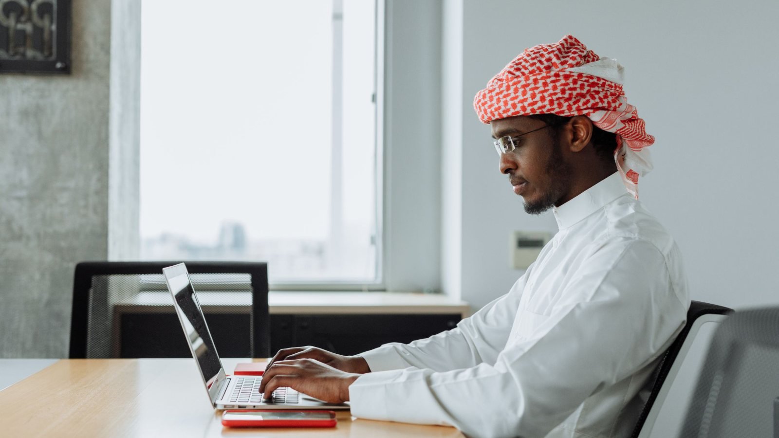 Middle Eastern man focused on work at a modern office desk with a laptop.