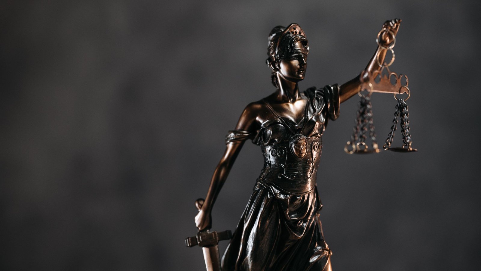 Detailed bronze Lady Justice statue with scales and sword against a dark background, symbolizing law and justice.