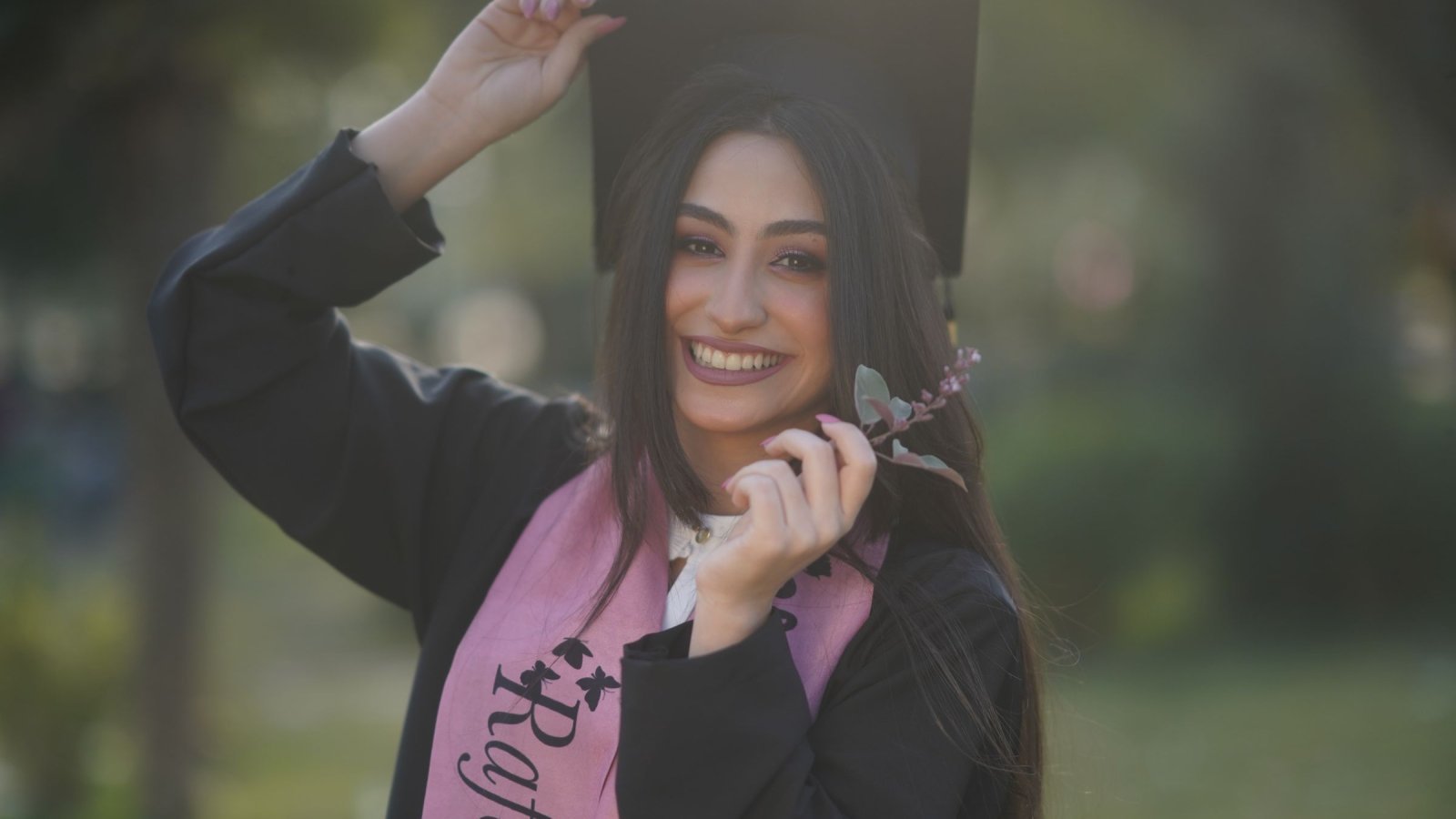 Smiling graduate in cap and gown celebrating her success outdoors