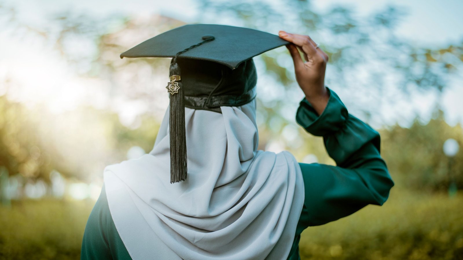 A hijabi woman celebrates graduation outdoors with an academic cap under the summer sky in Maldives.